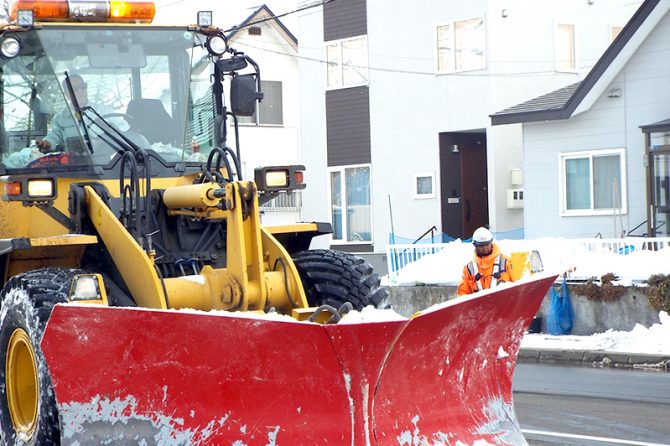 歩道の排雪作業中のドーザと警備員