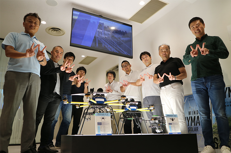 ジャパン・インフラ・ウェイマークの社員とともにポーズを決める春田さん(左端)。ハンドサインは「ウェイマーク」の「W」。
