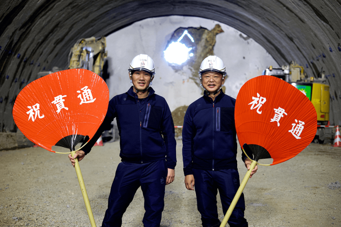 「祝貫通ウチワ」を持つ加藤広則さん（右）と下河太一さん