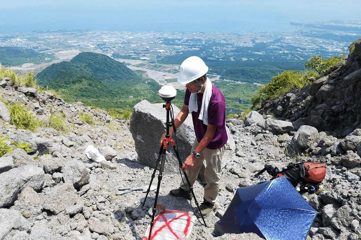 有明海を背後に、雲仙普賢岳山頂付近にて座標を計測中の北本さん(写真本人提供)
