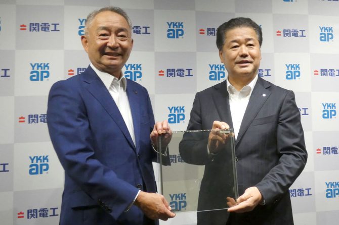 左から関電工の仲摩俊男社長、YKK APの魚津彰社長（中央に試作品のガラス型ペロブスカイトを持つ）