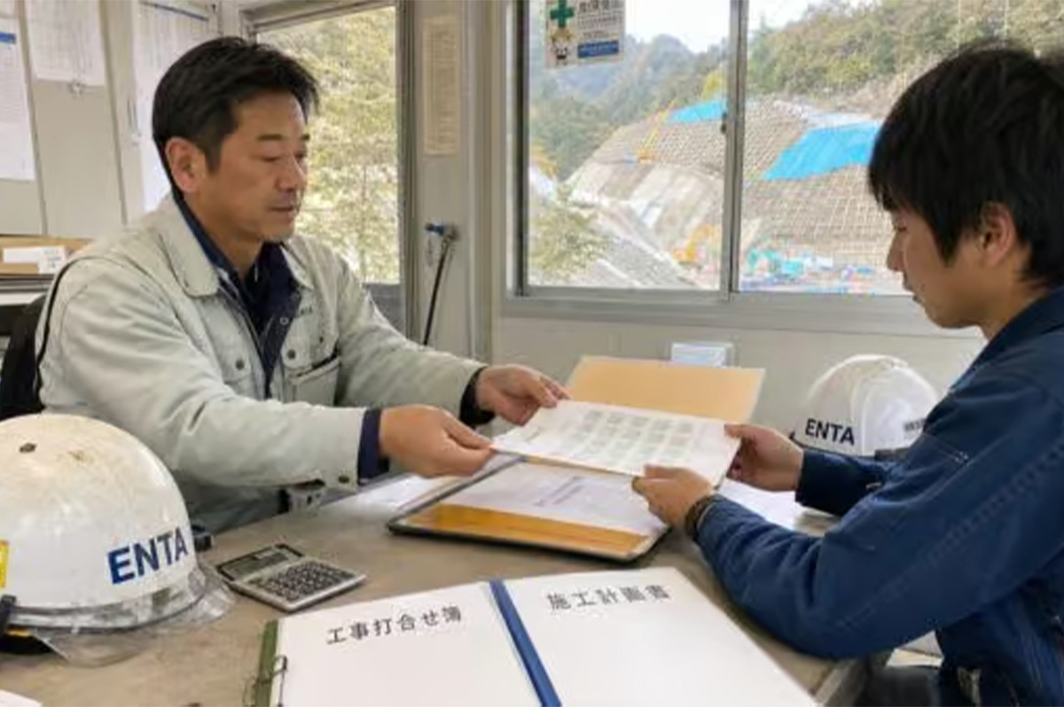 建設業退職金共済の共済証紙を入れたファイルを開きながら、若手の下請現場担当者に証紙を手渡している