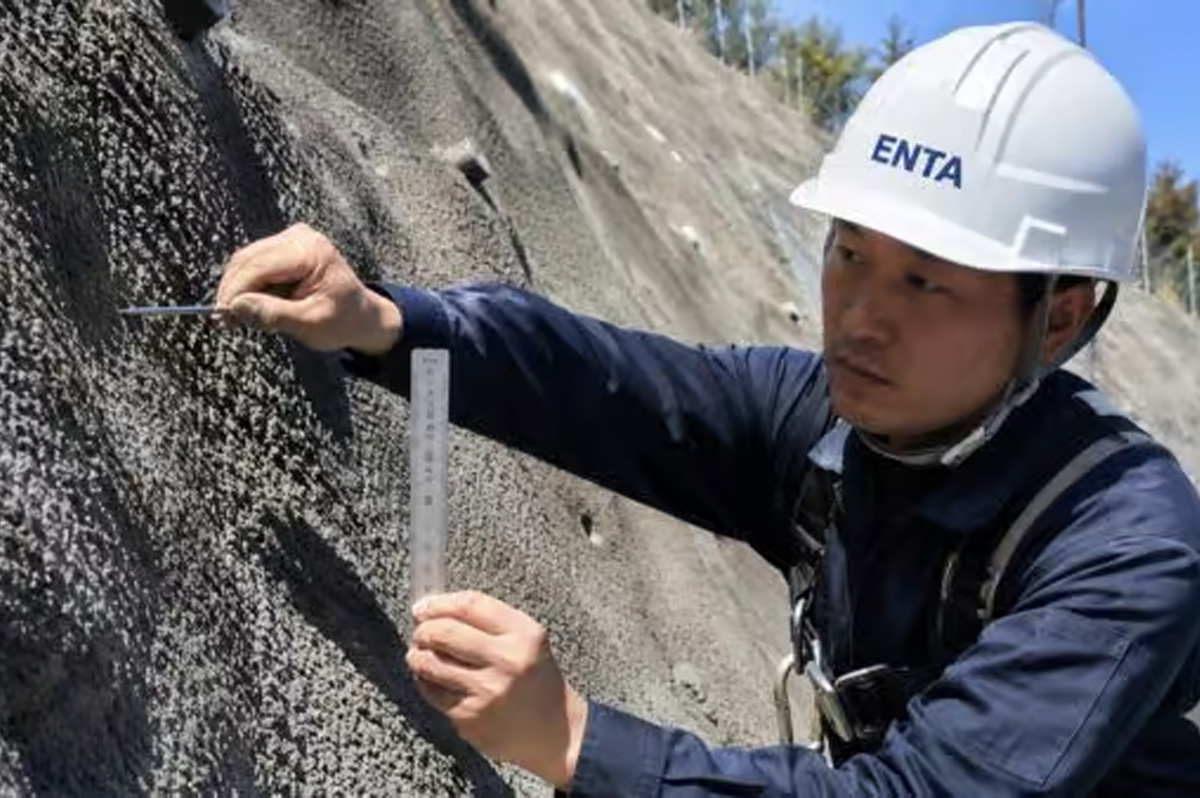 吹付モルタル法面の厚さを検尺ピンで測定している